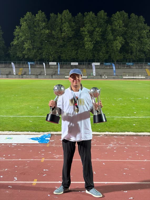 Jai Agarwal holding two trophies on the running track at night